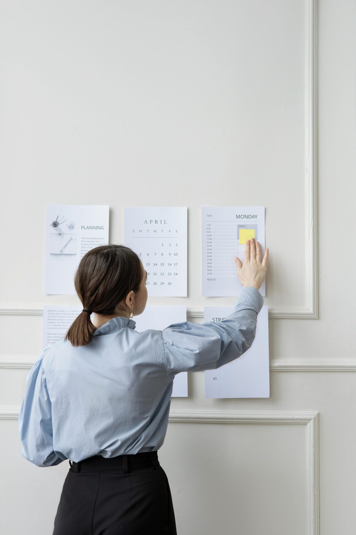 A woman facing away from the camera is looking at calendars and planning charts